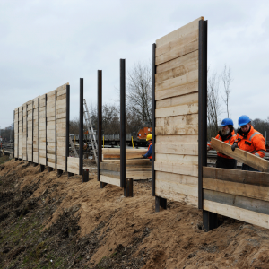 Arbeiter errichten eine Holzspundwand entlang der Baustelle.