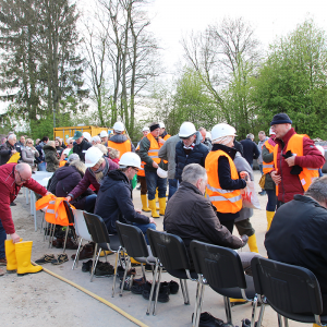 Eine Gruppe von Menschen legt Baustellenhelme, Warnwesten und Gummistiefel an.