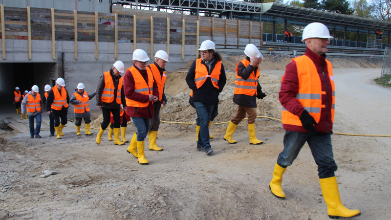 Eine Gruppe von Menschen mit Bauhelmen, Gummistiefeln und Warnwesten läuft über die Baustelle der U-Oldenfelde.