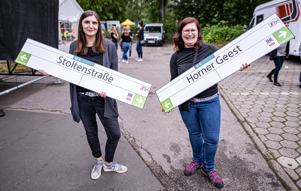 Zwei Personen halten Haltestellenschilder mit der Aufschrift "Stoltenstraße" und "Horner Geest" im Arm.