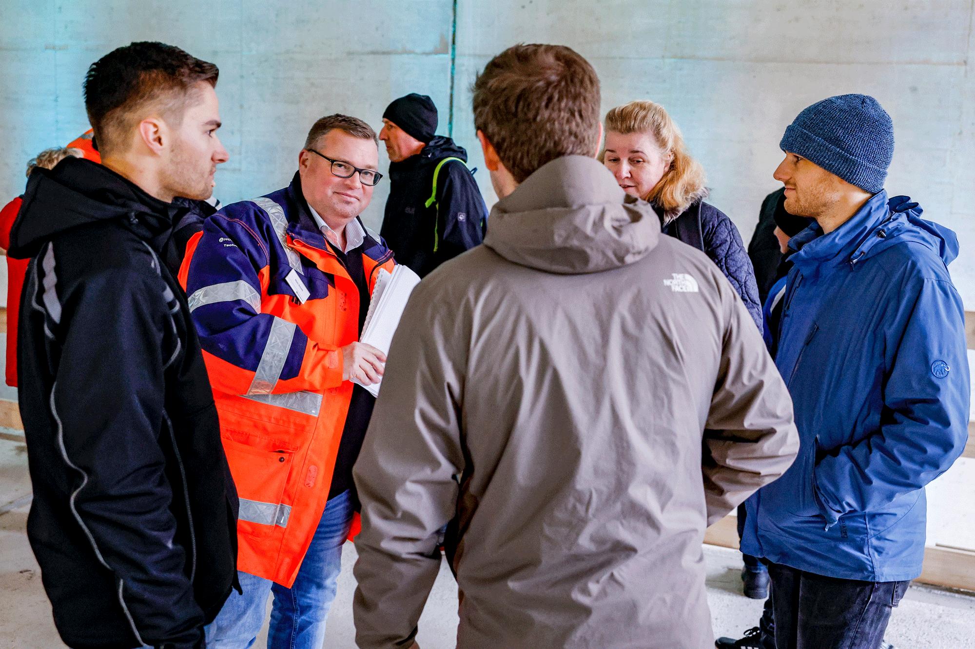 Eine kleine Gruppe von Menschen unterhält sich. Der Projektleiter trägt eine Orangene Arbeitsjacke.