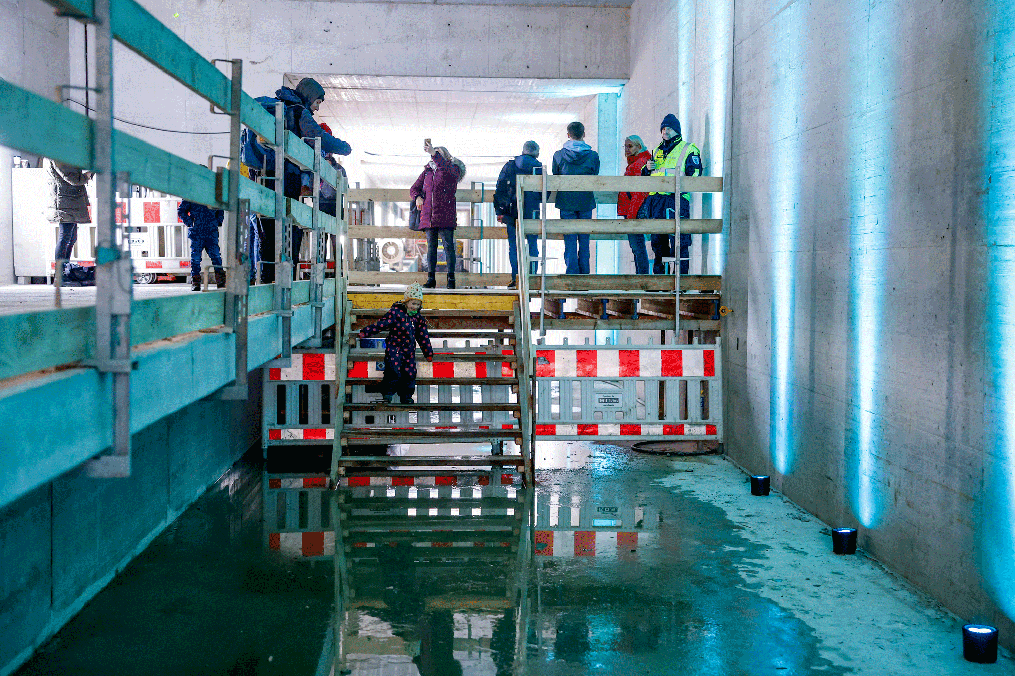 Im Rohbau des Tunnels: Menschen schauen sich um, ein kleines Kind geht eine kurze Treppe runter.