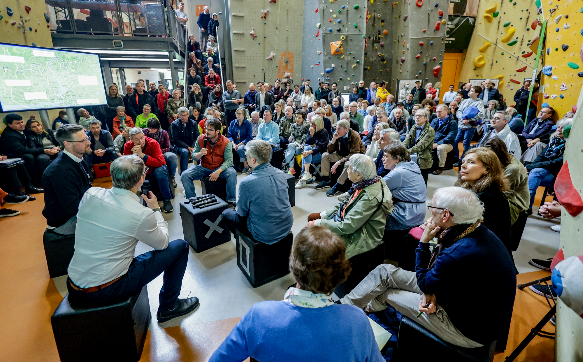 Veranstaltung in einer Kletterhalle, Menschen sitzen im Halbkreis um einen Redner im Mittelpunkt. 