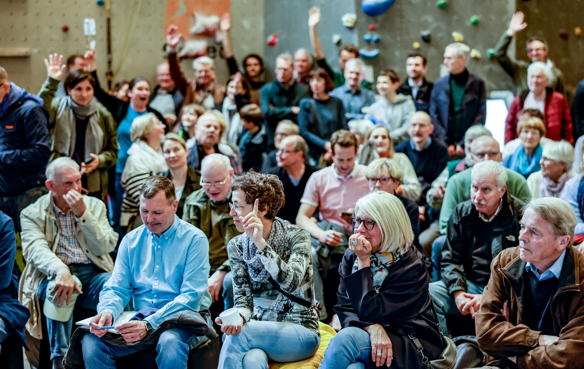 Foto von Publikum bei einer Veranstaltung, einige Menschen heben die Hand. 