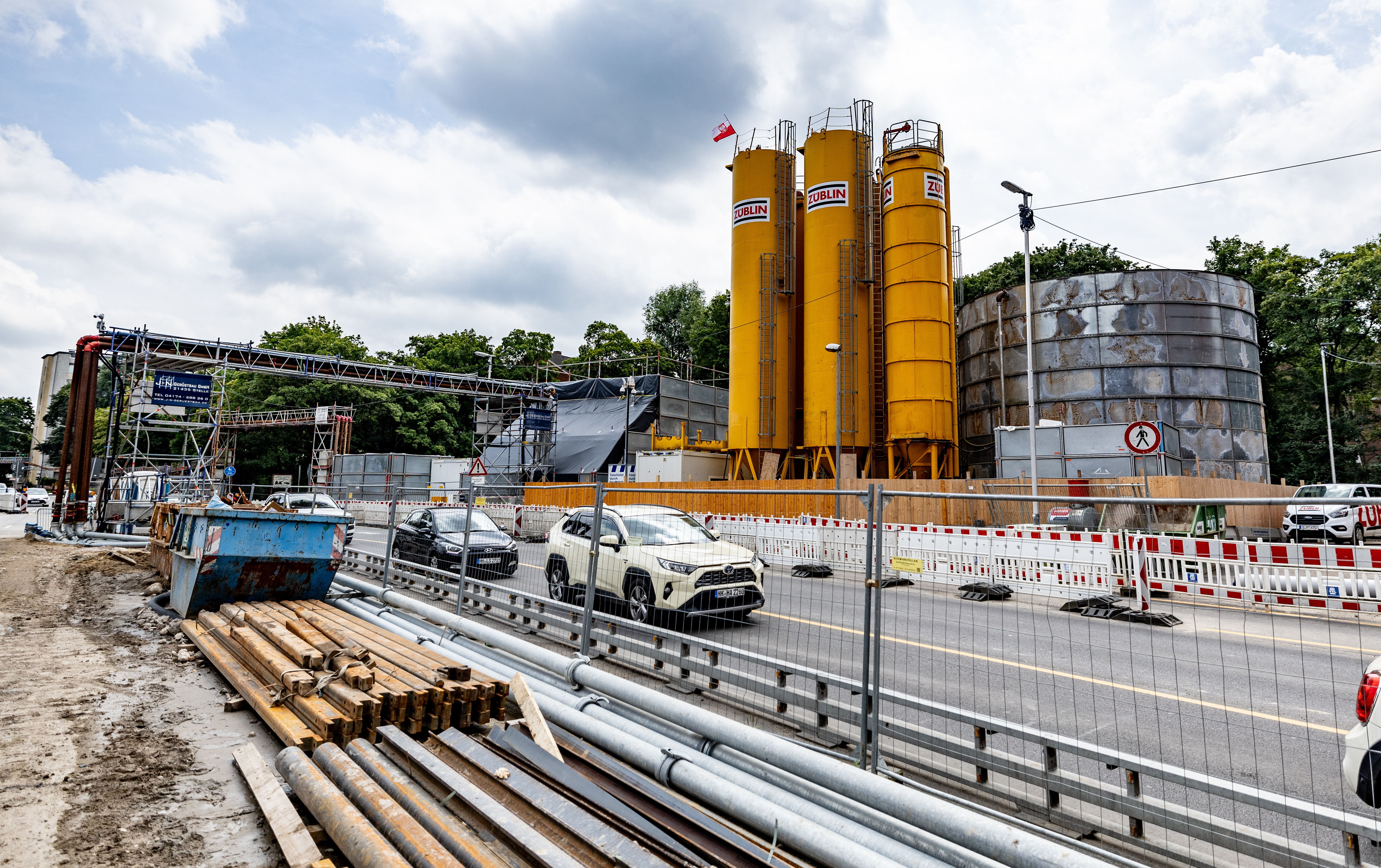 Blick von der Baustelle auf die Straße, im Hintergrund hohe Tanks. 