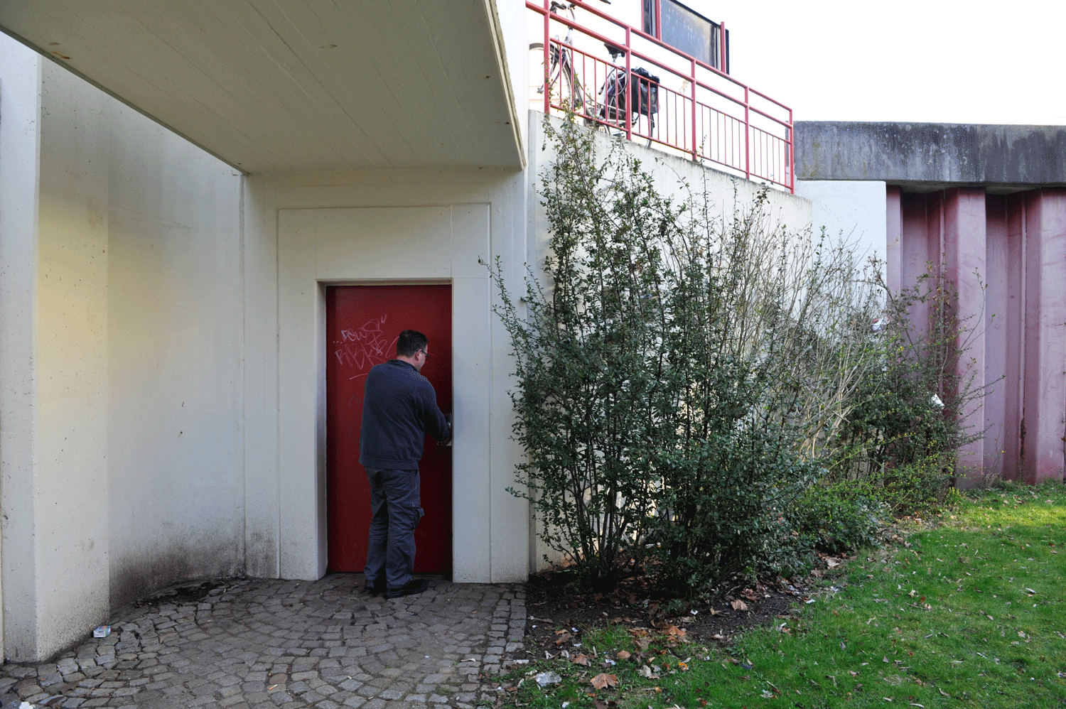 Eine rote Tür, unter einer Fußgänger-Überführung, wird von einer Person aufgeschlossen.