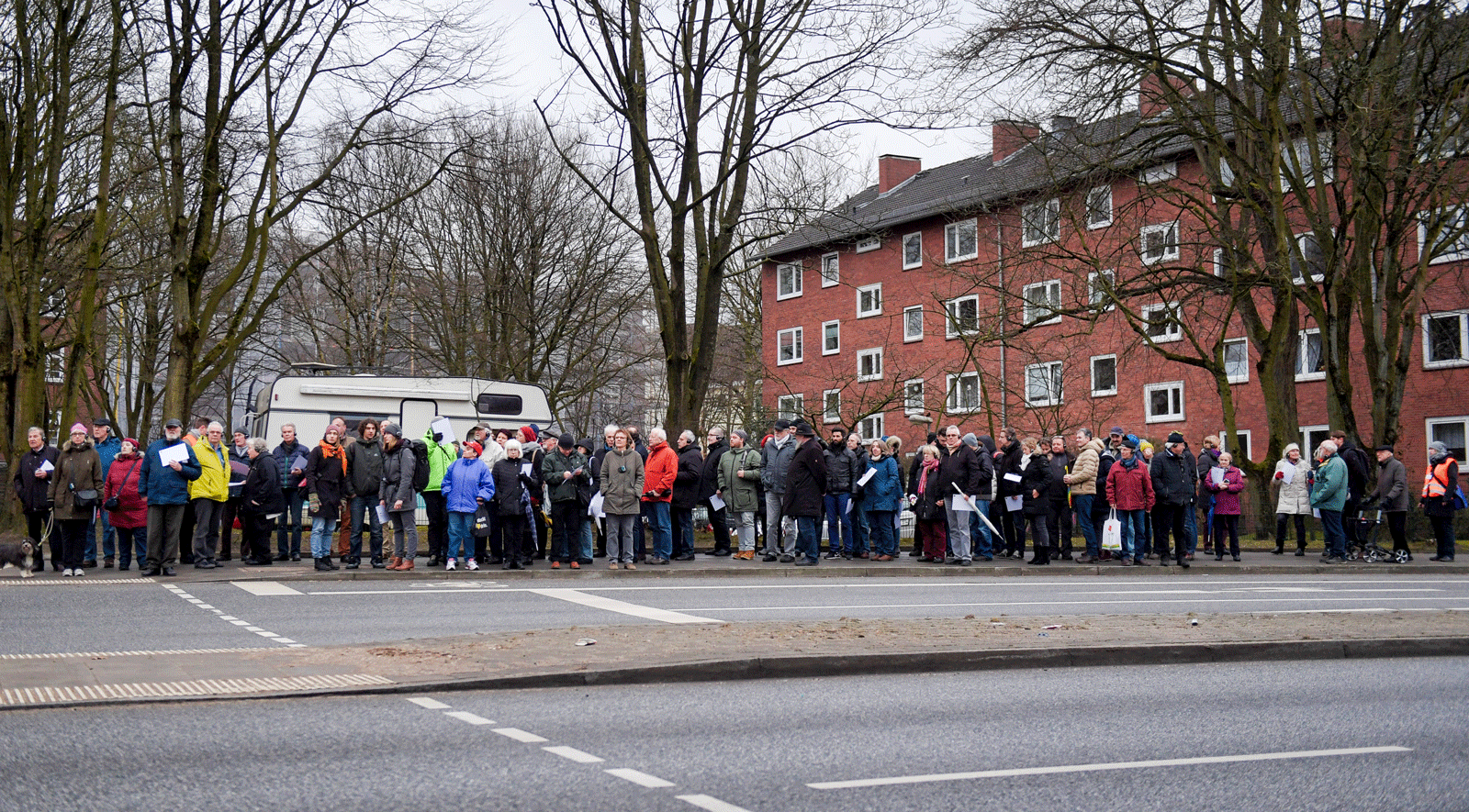 Menschen in Winterjacken drängen sich auf einem Fußgängerstreifen einer Straße.