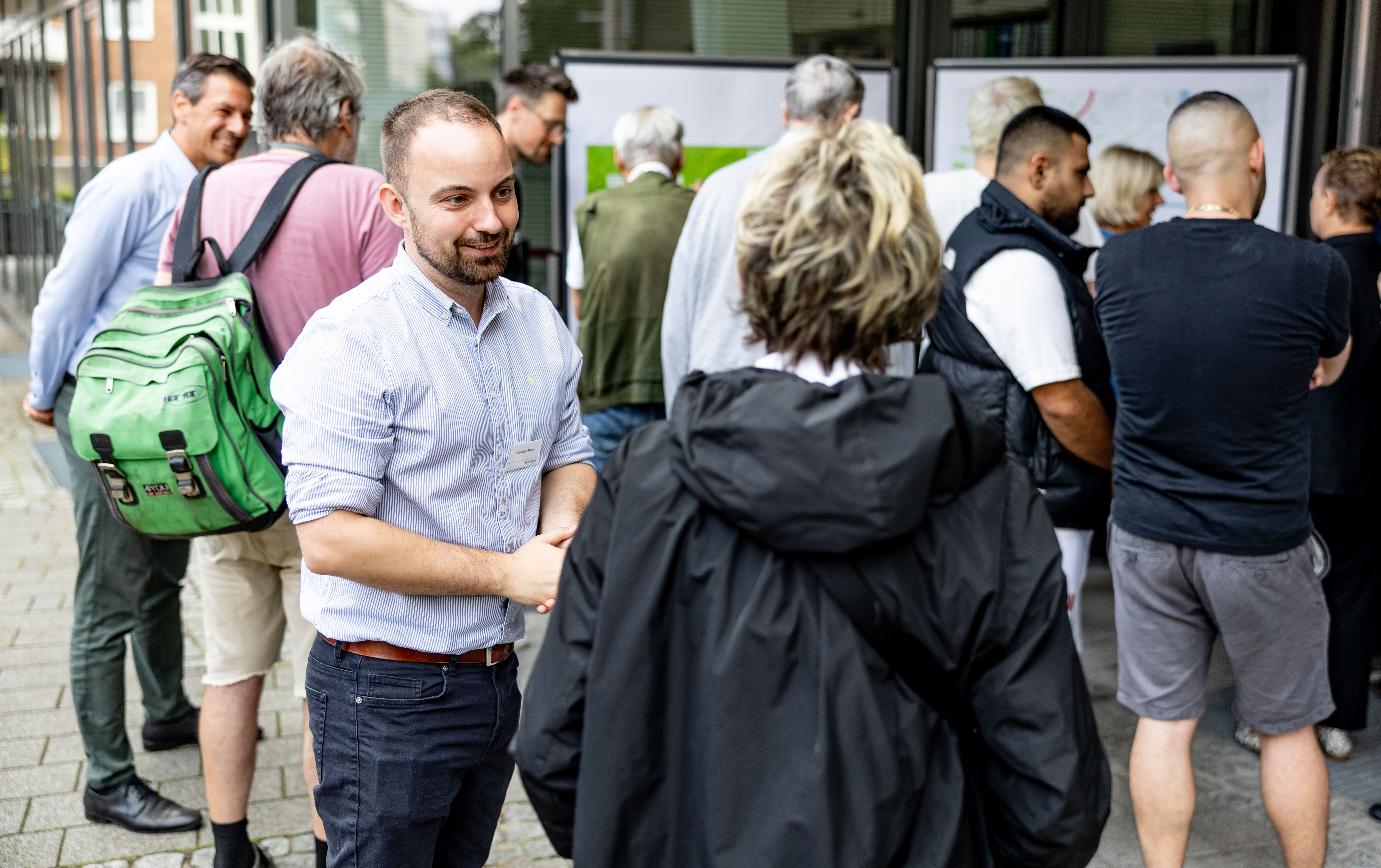 U5 Bauftragter Sebastian Meyer spricht mit einer Person. Im Hintergrund schauen sich andere Menschen Infoplakate an.