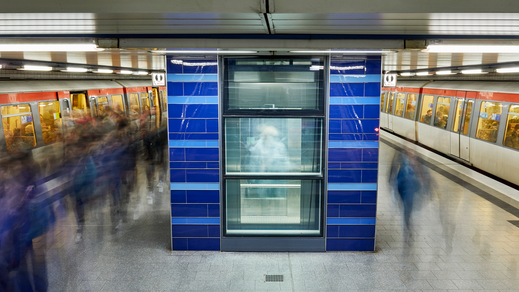 Bestehender Bahnsteig Horner Rennbahn, in der Mitte ein Fahrstuhl, links und rechts U-Bahnen und Menschen