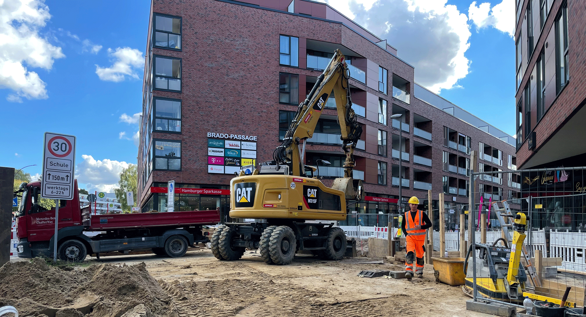 Bagger steht auf der Baustelle am Bramfelder Dorfplatz, im Hintergrund das EKZ