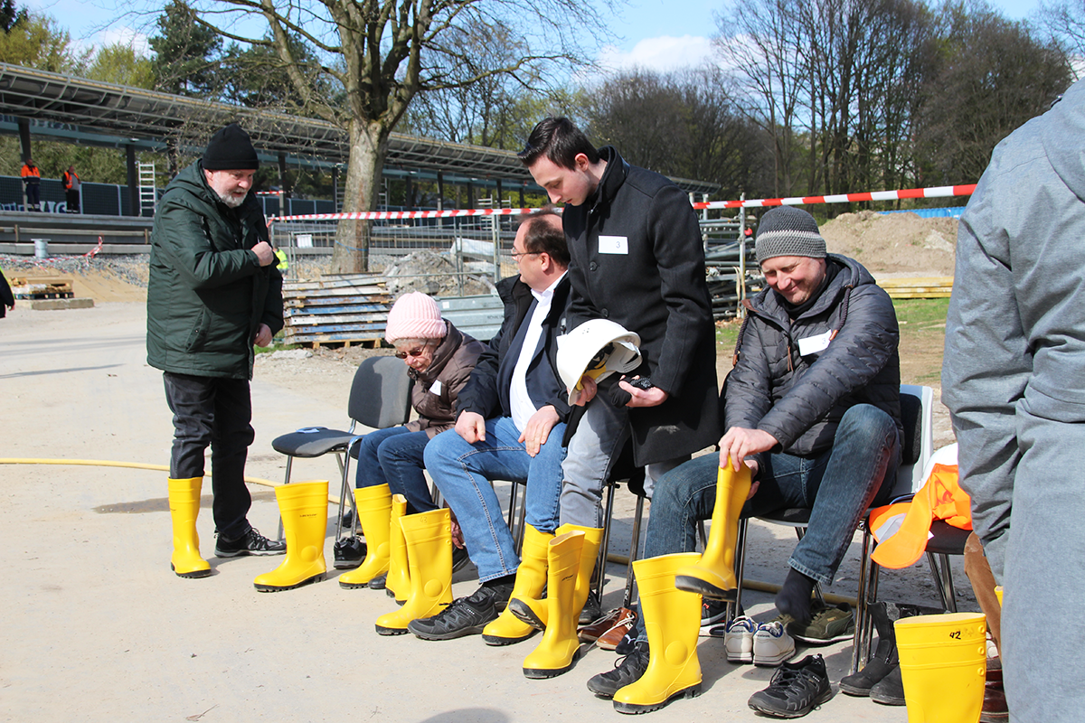 Eine Gruppe von Menschen zieht sich gelbe Gummistiefel an.