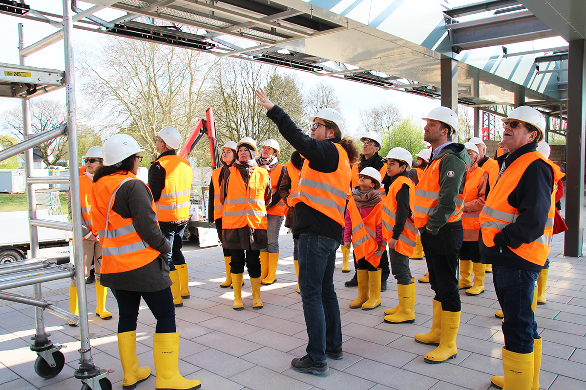 HOCHBAHN-Projektleiter Volker Schmidt deutet vor einer Gruppe Interessierter in Richtung des zukünftigen Bahnsteigdachs.