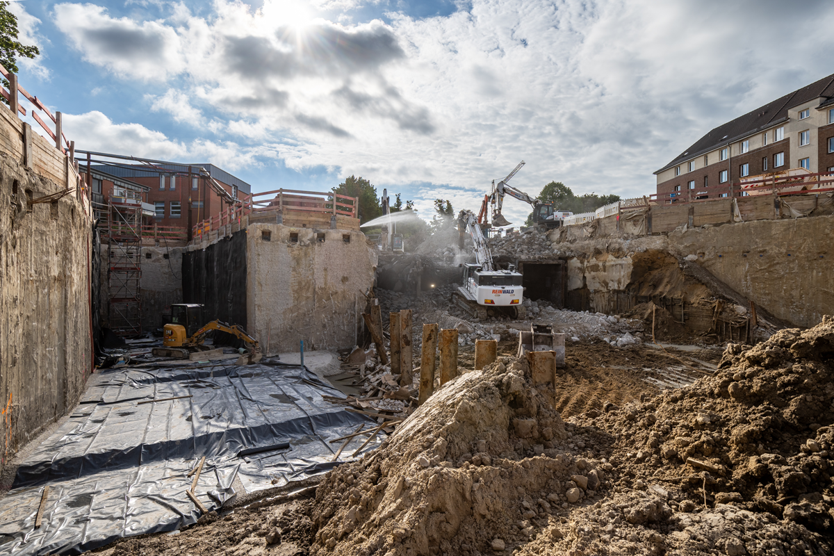 Links neben dem Abbruch ist die Baugrube bereits fertig ausgehoben. Hier führt später der U4-Tunnel Richtung Manshardtstraße weiter. Im nächsten Schritt werden hier die Tunnelwände  gebaut.