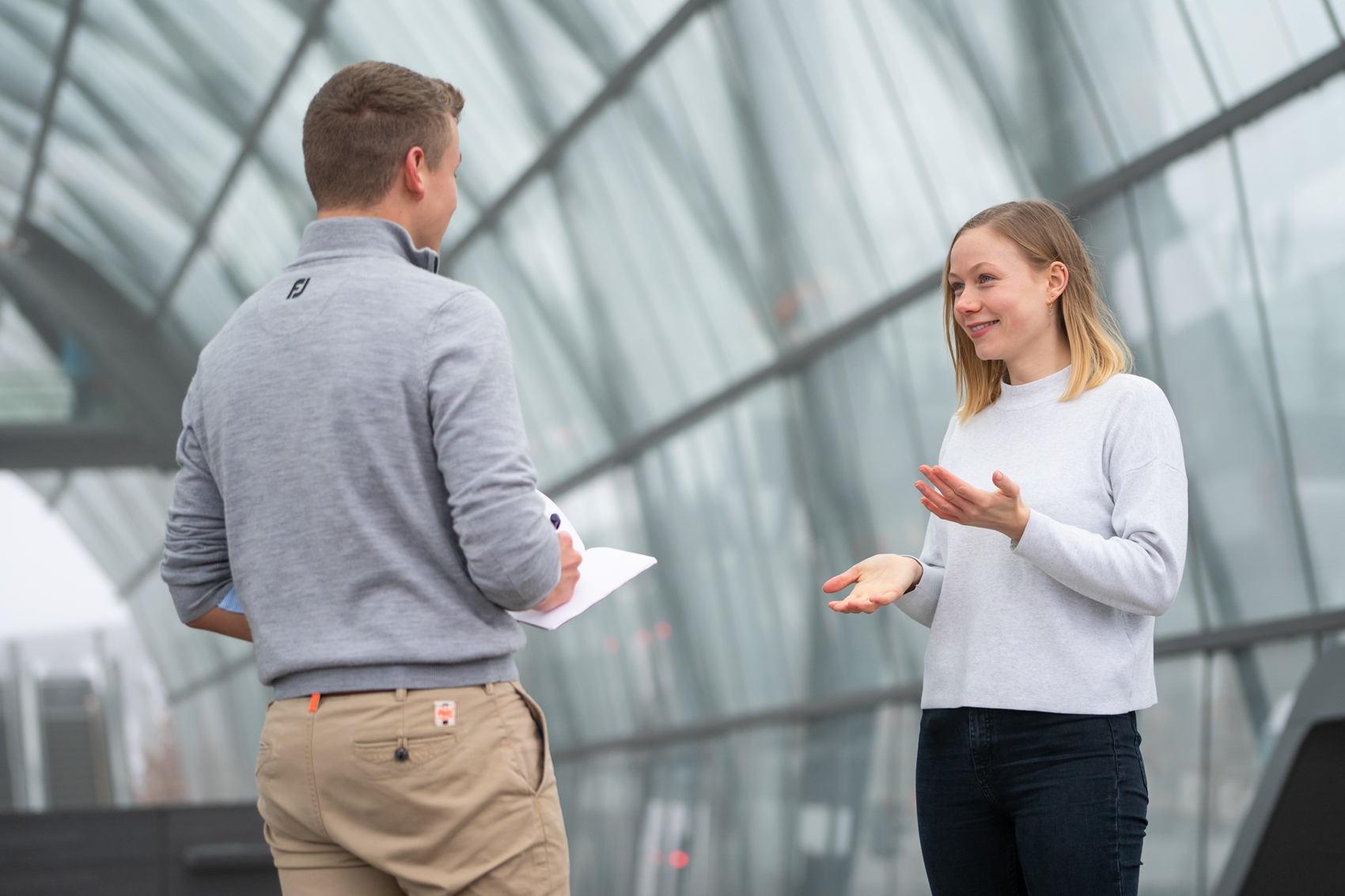 Mitarbeiterin Lena Steinat steht an der Haltestelle Elbbrücken gegenüber einer anderen Person, die nur von hinten zu sehen ist. Die beiden sind im Gespräch.