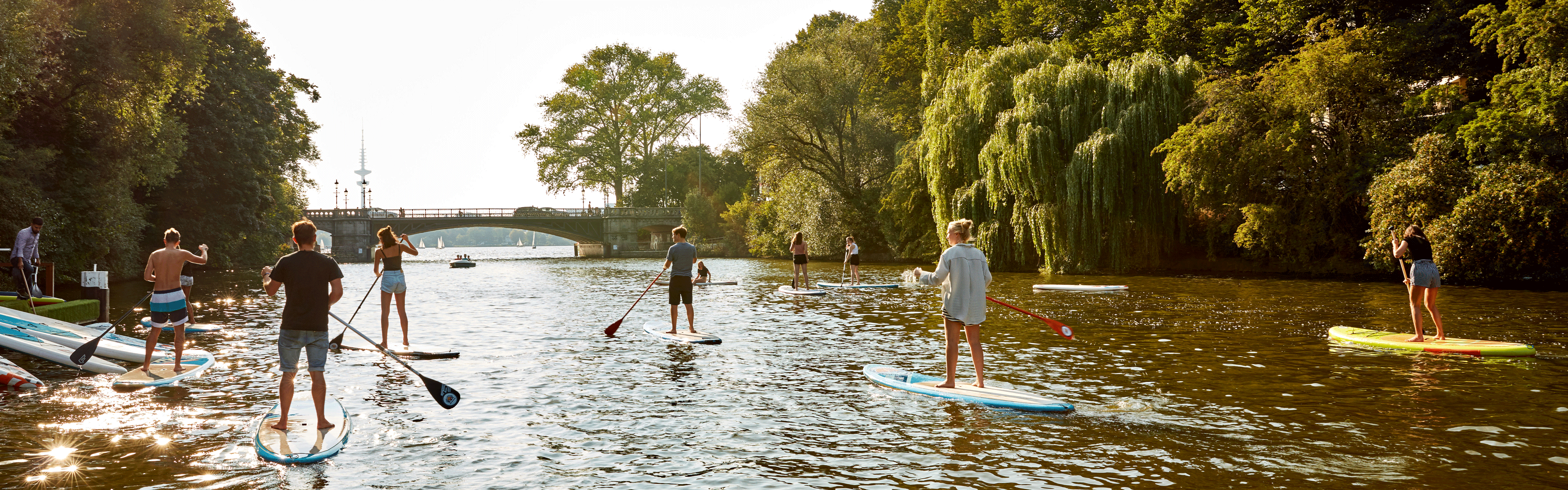 Mehrere Menschen auf Standup-Paddles auf einem Alsterkanal. 