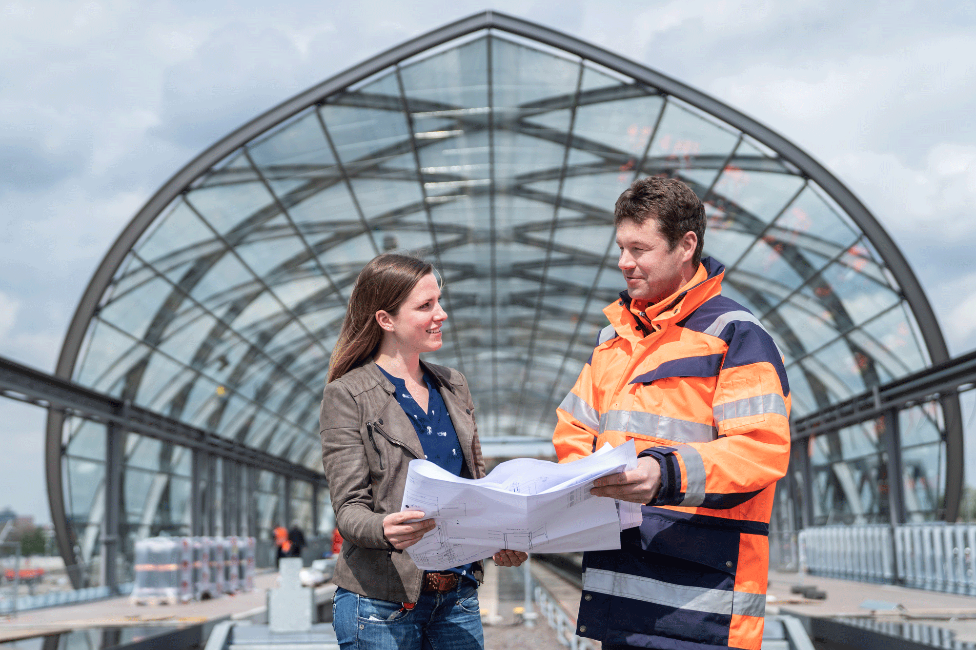 Zwei Mitarbeitende stehen an der Haltestelle Elbbrücken, halten gemeinsam einen Plan in der Hand. 