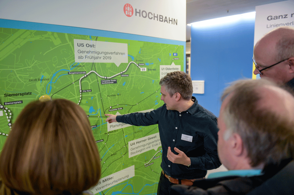 Ein Mitarbeiter der HOCHBAHN deutet auf eine Stadtkarte mit geplantem Streckenverlauf der U5.