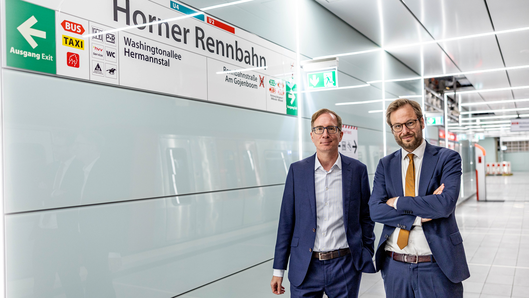 Senator Anjes Tjarks und Vorstandsvorsitzender Robert Henrich gemeinsam an der neuen Haltestelle Horner Rennbahn unter dem Haltestellenschild. 