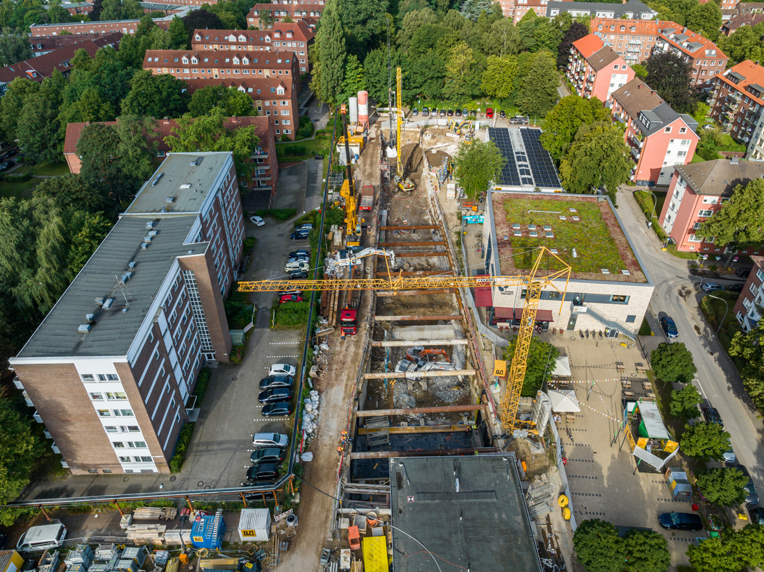 Direkt vor der Bestandshaltestelle (dunkles Dach) verbreitert sich die Baugrube, da an dieser Stelle zukünftig drei Tunnel nebeneinander verlaufen.