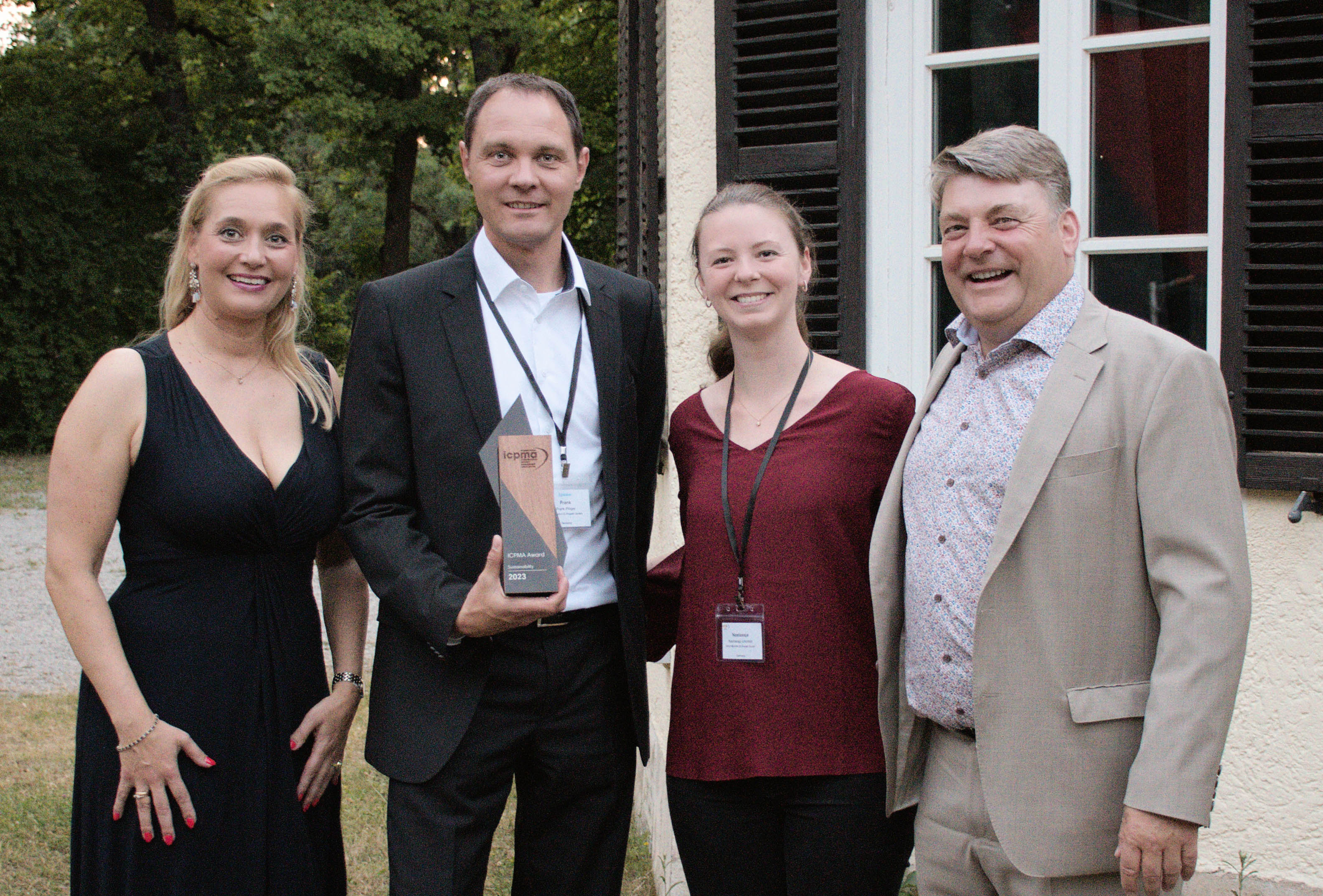 Vier Personen lächeln in die Kamera, eine Person hält einen Award in der Hand.