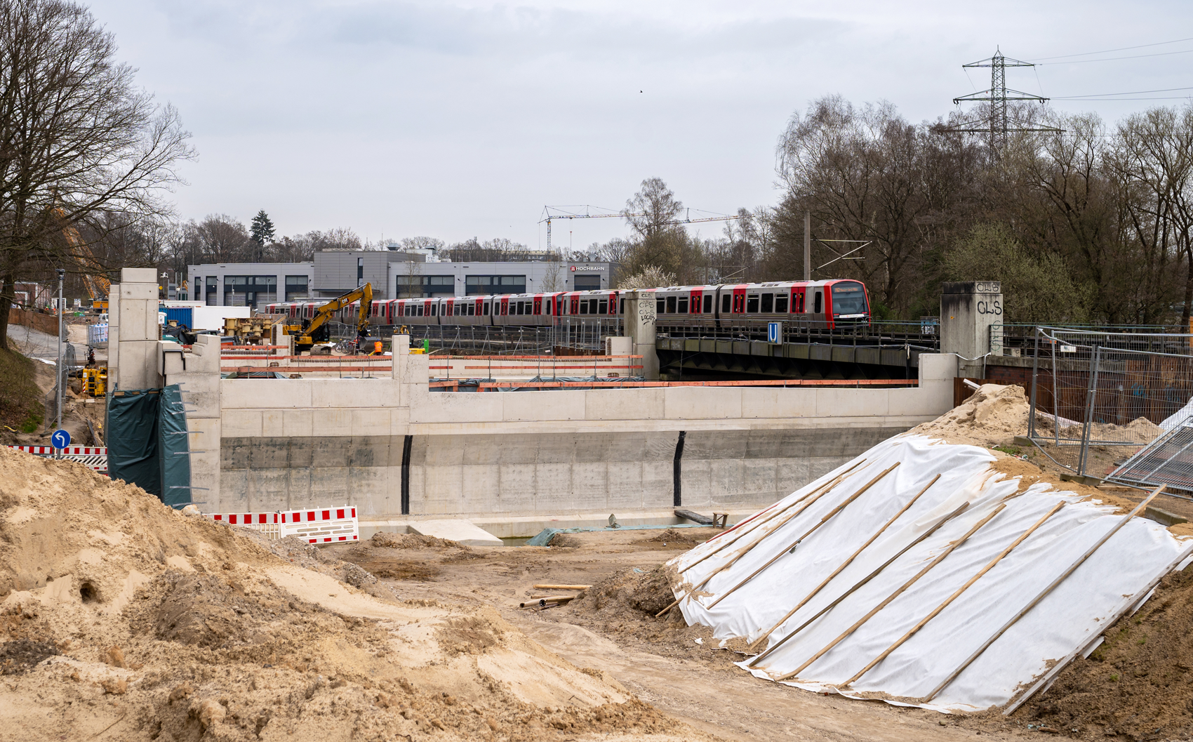 Von der Baustelle Blick auf die Widerlager Brücke U-Bahn Sengelmannstraße. Ein DT5 fährt im Hintergrund in die Station. 