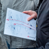Eine Person trägt eine laminierte Ortskarte mit Markierten Bereichen bei sich.