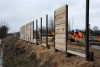Arbeiter errichten eine Holzspundwand entlang der Baustelle.